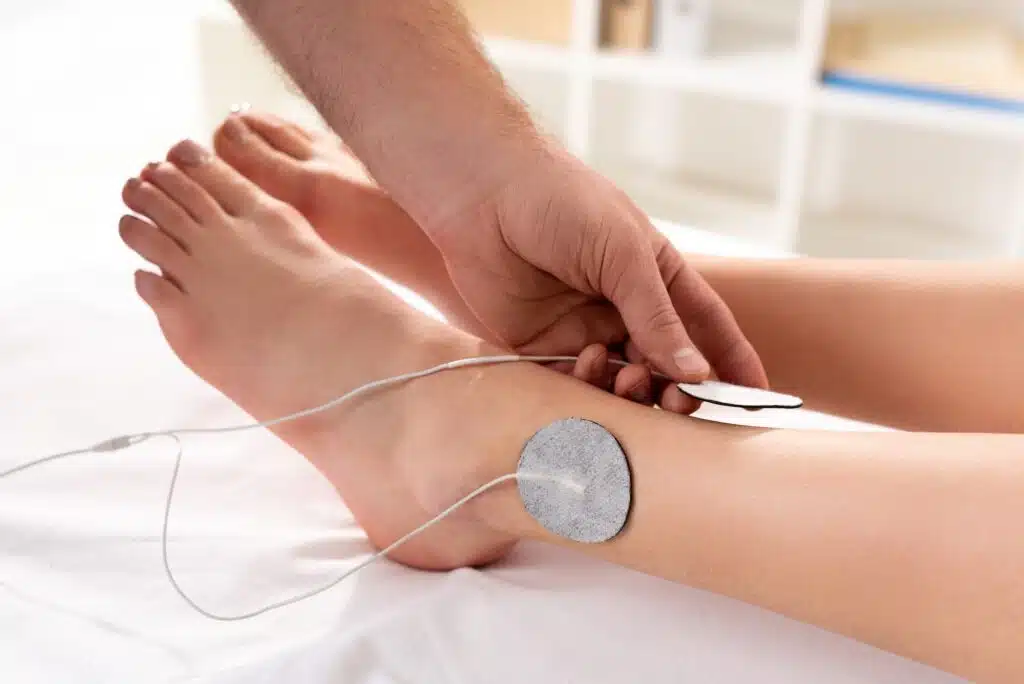 Ausschnitt eines Physiotheraüueten, der eine Elektrode an das Bein eines Patienten hält, während einer Elektrodenbehandlung in einer Massagepraxis