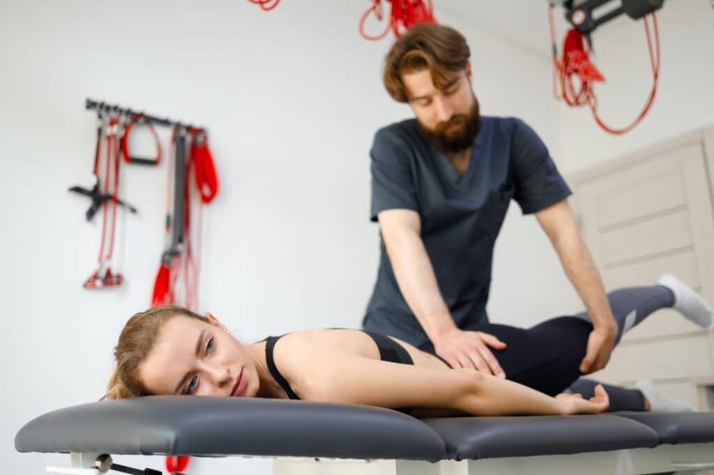 Manuelle Therapie: Ein Physiotherapeut massiert den Hüftbeuger einer jungen Frau