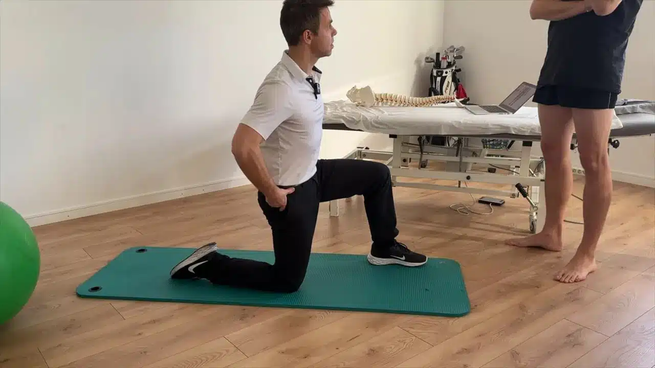Golf Physiotherapie: Wie gezielte Physiotherapie deinen Golfschwung verbessert 1 Golfphysiotherapie Therapeut demonstriert kniende Quadrizeps‑Dehnung auf Matte, Hand am Becken zur Kontrolle der Beckenstellung